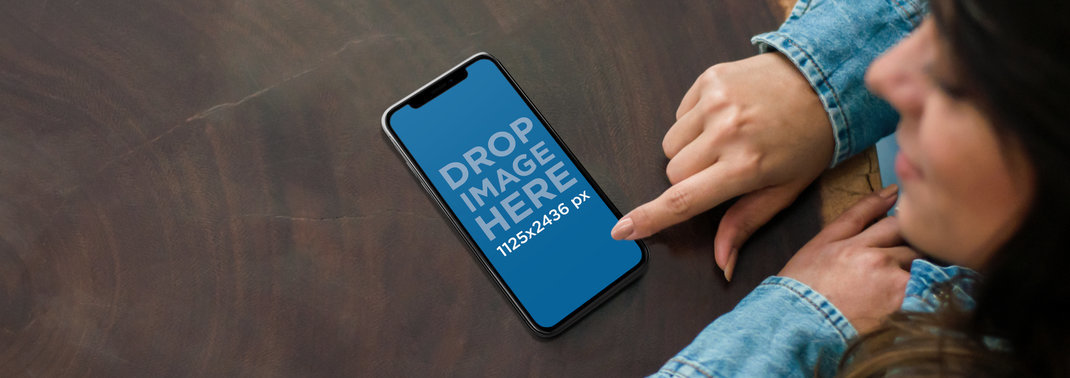 Mockup of a Young Woman using an iPhone 11 Pro on a Wooden Table