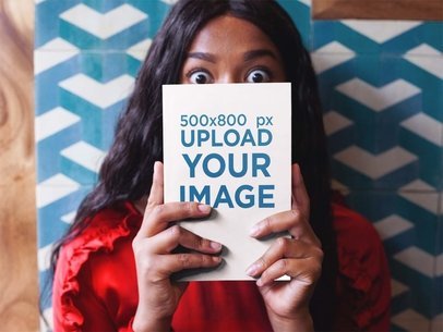Surprised Woman Holding a Book Mockup While Against a Tiles Wall a17345