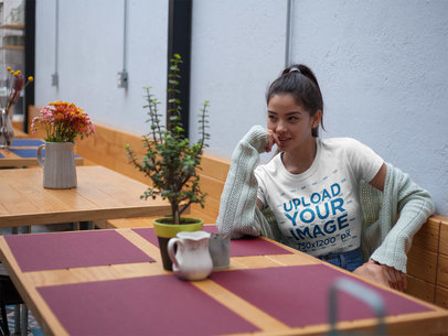 Pretty Girl Wearing a Round Neck Tee Mockup While Sitting on a Wood Table at a Cafe a17472