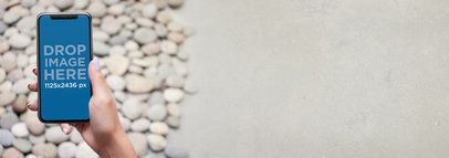 iPhone X Mockup Being Held by a Girl Against a Pebble Floor a17542