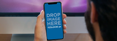 Man Holding an iPhone X Mockup Against a TV a17616