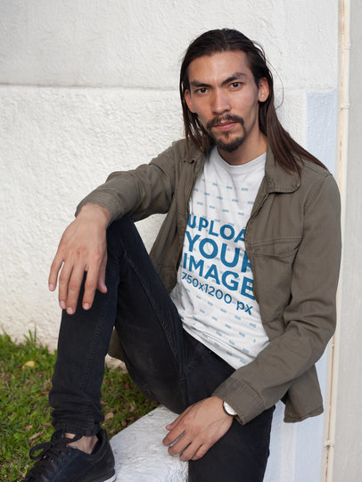 Asian Man Wearing a Round Neck Tee Mockup Sitting Against a Wall