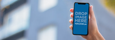 Man Holding an iPhone 11 Pro Mockup Against a Blurry Building