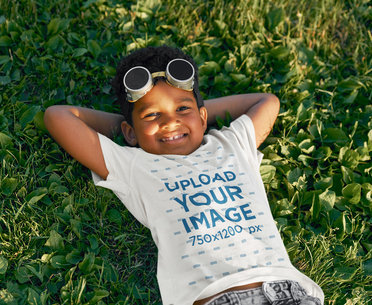 T-Shirt Mockup of a Smiling Boy Laying on the Grass with Toy Plane Glasses