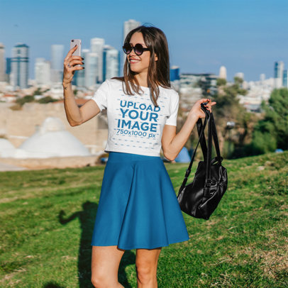 Crop Top Mockup Featuring a Happy Young Woman Taking a Selfie at a City Park 