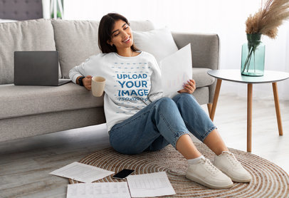 Sweatshirt Mockup Featuring a Smiling Woman Sitting on the Floor and Looking at a Paper