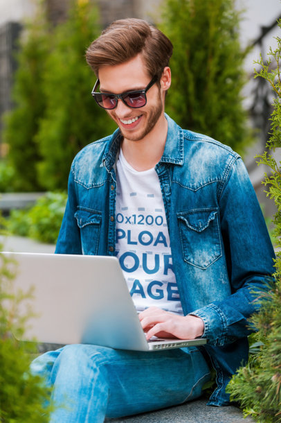 T-Shirt Mockup of a Smiling Man with Sunglasses Working on His Laptop