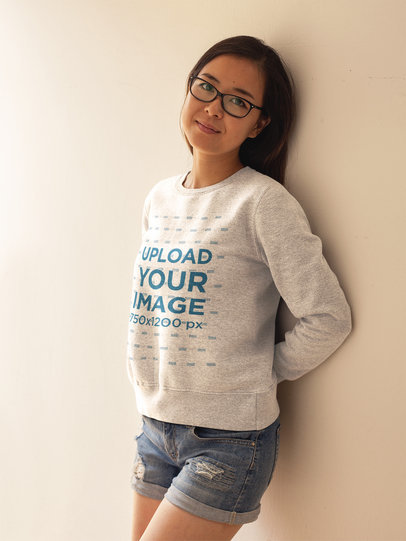 Cute Girl with Glasses Wearing a Crewneck Sweatshirt Template While Lying Against a White Wall a17609