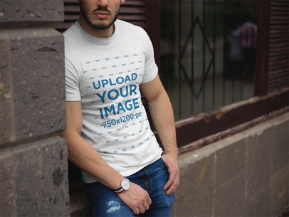 Bearded Man Wearing a T-Shirt Mockup While Lying Against a Church Wall