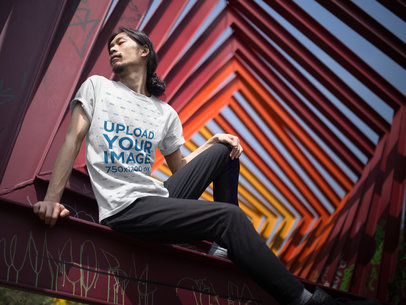 Long Hair Asian Man Wearing a T-Shirt Mockup While Sitting on a Red Urban Structure