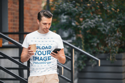 Round-Neck T-Shirt Mockup of a Man With a Coffee and Checking His Phone