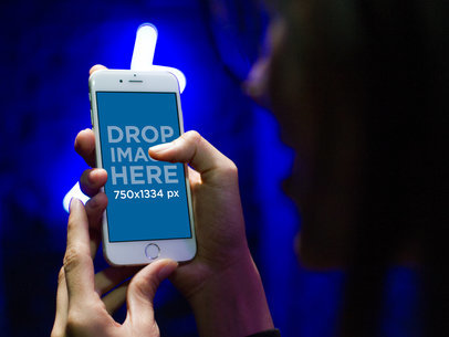Woman Holding a White iPhone Mockup Against a Wall with Neon Lights