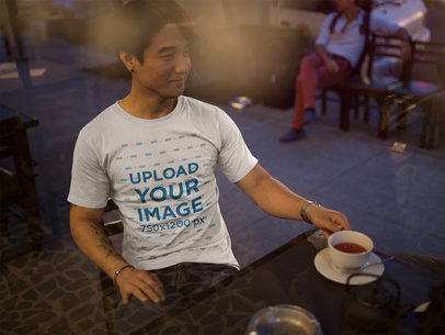 Through the Window Mockup of an Asian Man Wearing a Tshirt at a Cafe