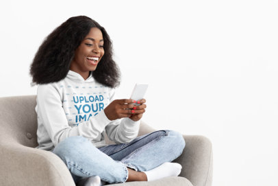 Pullover Hoodie Mockup of a Happy Woman Texting on Her Mobile Phone