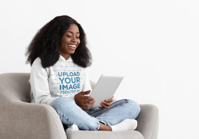 Pullover Hoodie Mockup of a Woman with a Tablet Sitting on an Armchair 