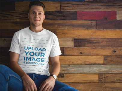 Man Wearing a Tshirt Mockup while Sitting Against a Wooden Wall