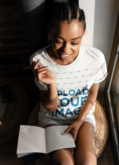T-Shirt Mockup of an Inspired Woman Writing Next to a Window