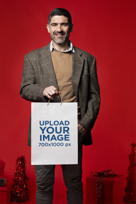 Mockup of a Bearded Man Holding a Gift Bag in a Studio with Christmas Decorations