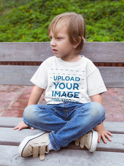 Sad Kid Wearing a Tshirt Mockup Sitting on a Bench