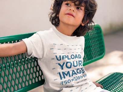 Boy Wearing a Tee Mockup Sitting on a Green Bench