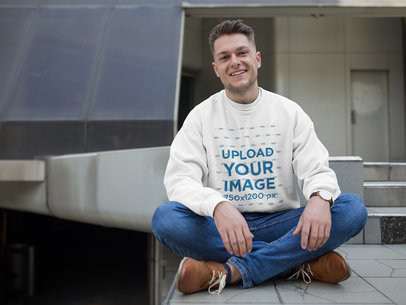 Happy Dude Wearing a Crew Neck Sweatshirt Template while Sitting Outside a Building