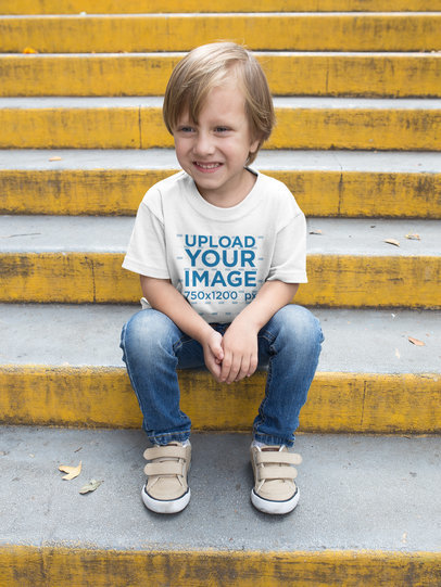 Happy Kid Wearing a Tshirt Mockup while Sitting on Yellow Concrete Stairs