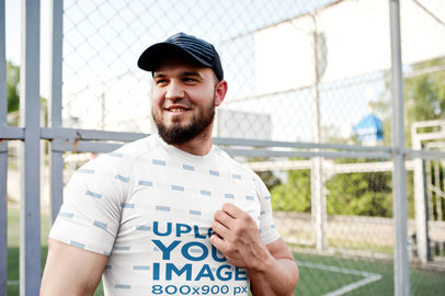 T-Shirt Mockup of a Muscular Man Posing in Front of a Soccer Field