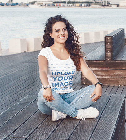 T-Shirt Mockup of a Curly-Haired Woman Sitting on a Wooden Platform