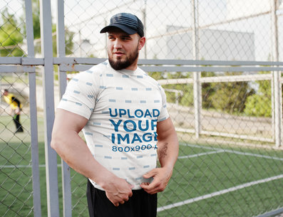 T-Shirt Mockup of a Muscular Man Posing by a Soccer Field