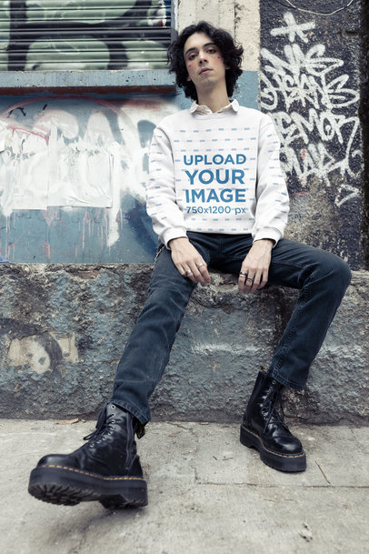 Sweatshirt Mockup Featuring an E-boy Sitting Against a Graffiti Wall