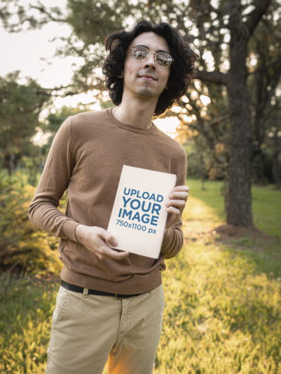 Mockup of a Smiling Man with Glasses Showing a Hard-Cover Book at a Garden