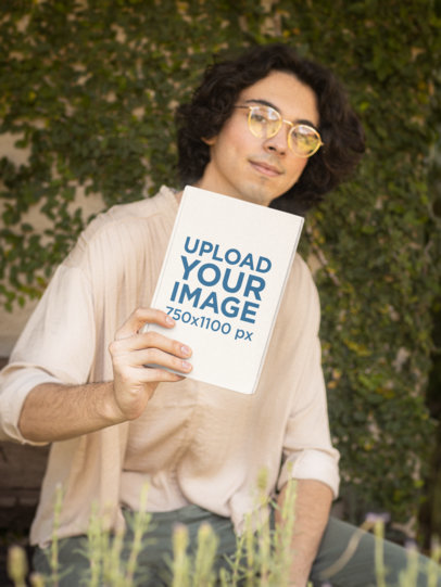 Mockup of a Man with Glasses Holding a Hard-Cover Book