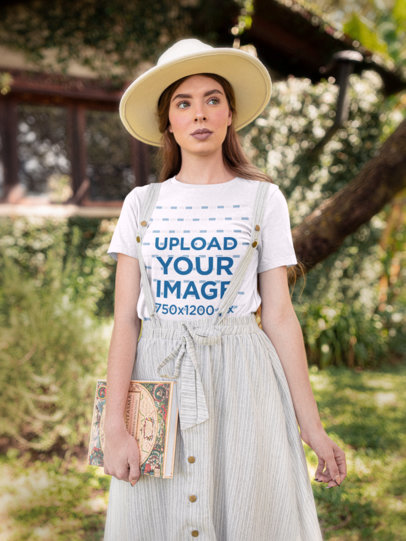 T-Shirt Mockup of a Woman with a Countryside Outfit Holding a Publication M18711