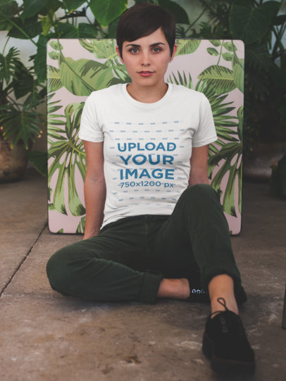 Woman Wearing a Tshirt Mockup While Sitting Against a Plants Printed Table