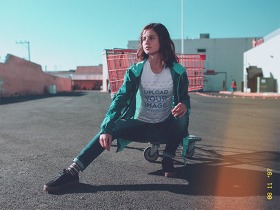 Woman Wearing a Tshirt Mockup and a Green Jacket While Sitting on a Cart base at a Parking Lot