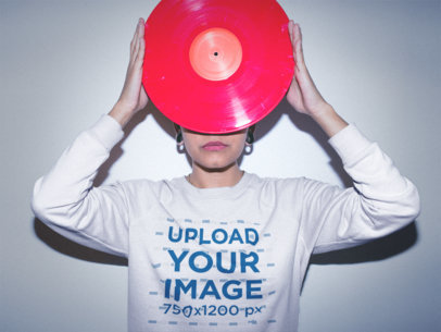 Woman Wearing a Crewneck Sweatshirt Mockup while Holding a Vinyl Against her Face
