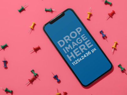 Mockup of an iPhone 11 Pro Lying on a Pink Surface Surrounded by Board Pins