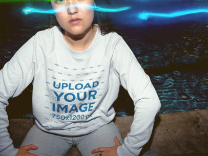Blue Lights on a Girl Wearing a Crewneck Sweater Mockup Sitting Down Near a Fountain a18858