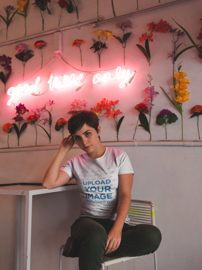 Short Haired Woman Wearing a Tshirt Mockup Sitting Near a Pink Neon Decoration