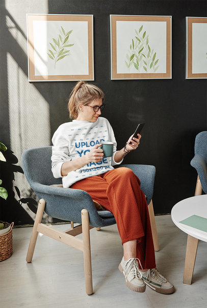 Sweatshirt Mockup Featuring a Woman Checking Her Phone While Drinking Tea