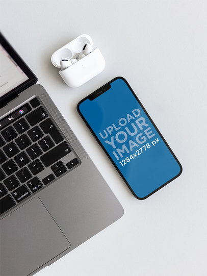 Mockup of an iPhone 12 Pro Max Placed by a Computer and Some Earbuds m21864