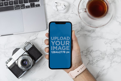 Mockup of a Photographer Holding an iPhone 12 Pro Max Over His Desk