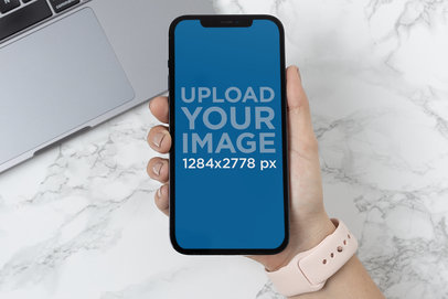 Mockup of a Woman Holding an iPhone 12 Pro Max over a Marble Surface