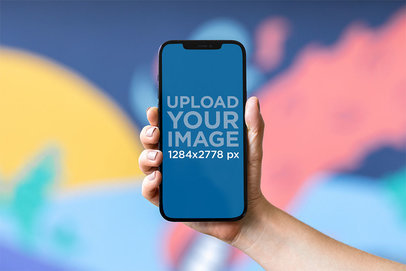 Mockup of a Hand Holding an iPhone in Front of a Colorful Wall m21956