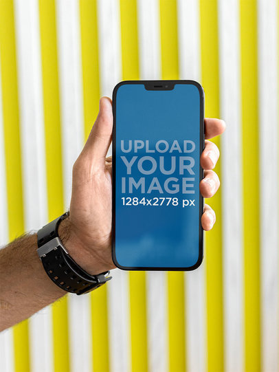 Mockup of a Man’s Hand Holding an iPhone 12 Pro Max Against a Striped Wall m21953