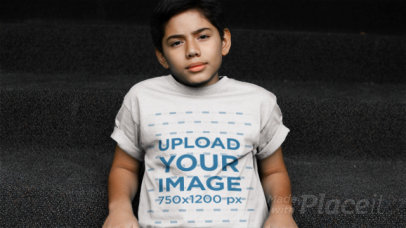 Young Boy Sitting on Some Stairs Wearing a Kid's T-Shirt Video Mockup