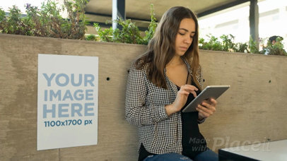 Young Business Woman Using An iPad With A Poster Video Mockup Besides Her