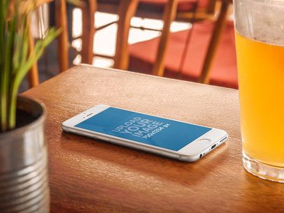 Mockup of an iPhone 6 on Wooden Table Next to a Beer