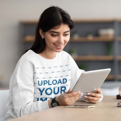 Sweatshirt Mockup of a Woman at a Table Holding a Tablet 