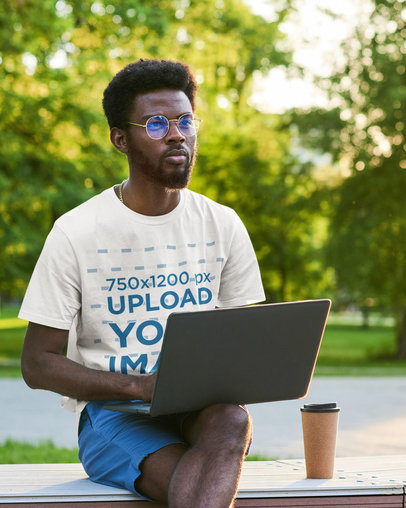 T-Shirt Mockup Featuring a Man With Glasses Using a Laptop